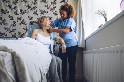 caregiver helping a senior woman get dressed in her bedroom