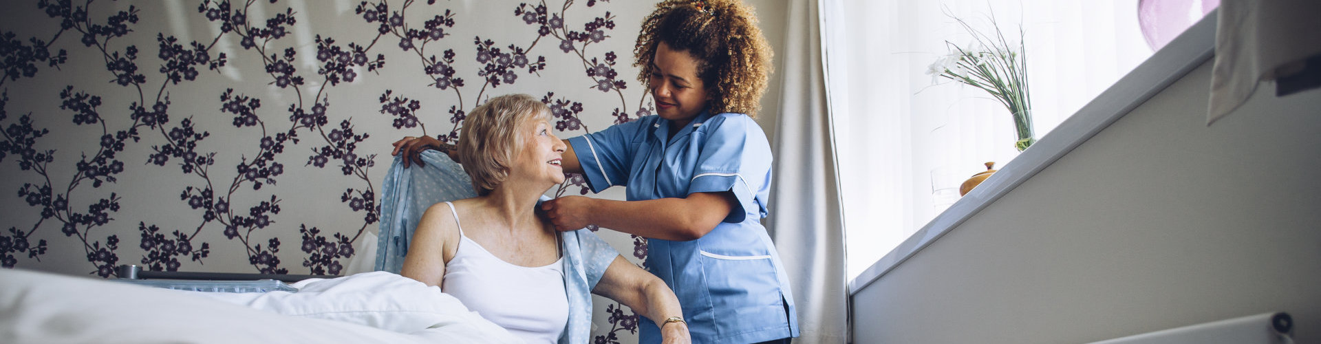 caregiver helping a senior woman get dressed in her bedroom